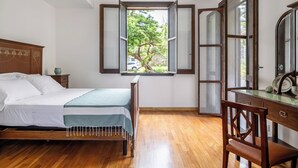 Une chambre à coucher avec un lit en bois, un bureau doté d’un miroir et une fenêtre dont les volets sont ouverts.