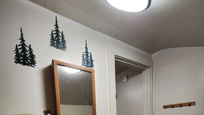 A bathroom with a white sink, a mirror, and a towel rack. There are three tree decals on the wall. - Secluded group of cottages close to town (Seward)