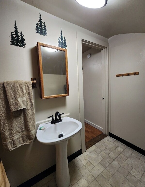 A bathroom with a white sink, a mirror, and a towel rack. There are three tree decals on the wall. - Secluded group of cottages close to town (Seward)
