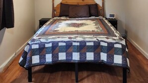 A bedroom with a wooden bed, a nightstand, and a small table. - Secluded group of cottages close to town (Seward)