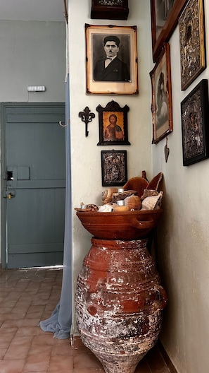A rustic interior with a large clay pot, a door, and several framed religious icons on the wall.