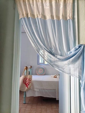 A room with a bed, a window, and a door with a sheer curtain.