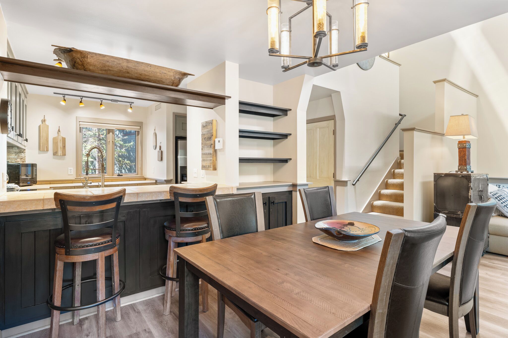 A modern kitchen with a wooden island, bar stools, and a dining table with chairs.