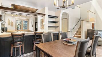 A modern kitchen with a wooden island, bar stools, and a dining table with chairs.