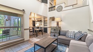 A spacious living area with a sofa, coffee table, and a dining table. A kitchen is visible in the background, and there is a large window providing natural light. - Ss1902-1 (Keystone)