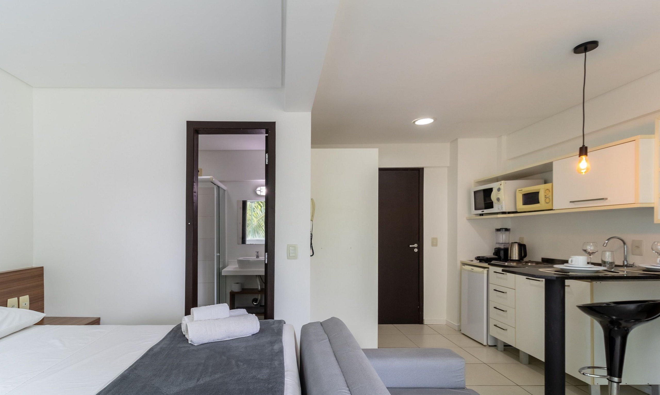 Een moderne hotelkamer met een bed, een bank, een kitchenette en een badkamer, zichtbaar door een geopende deur.