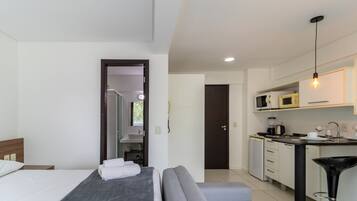 Een moderne hotelkamer met een bed, een bank, een kitchenette en een badkamer, zichtbaar door een geopende deur.