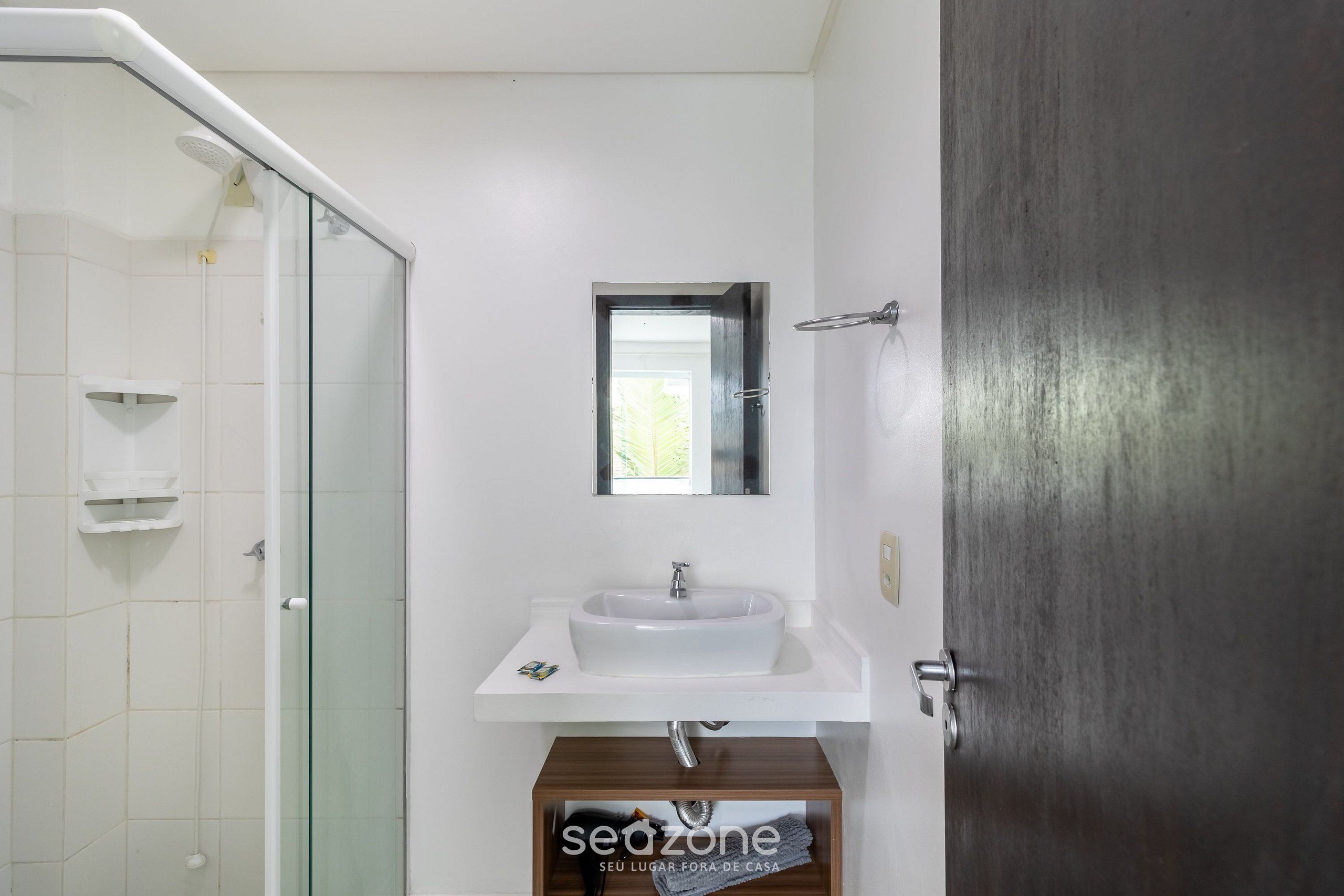 Un baño con cabina de ducha de vidrio, un lavamanos blanco con espejo arriba y un mueble de madera debajo.