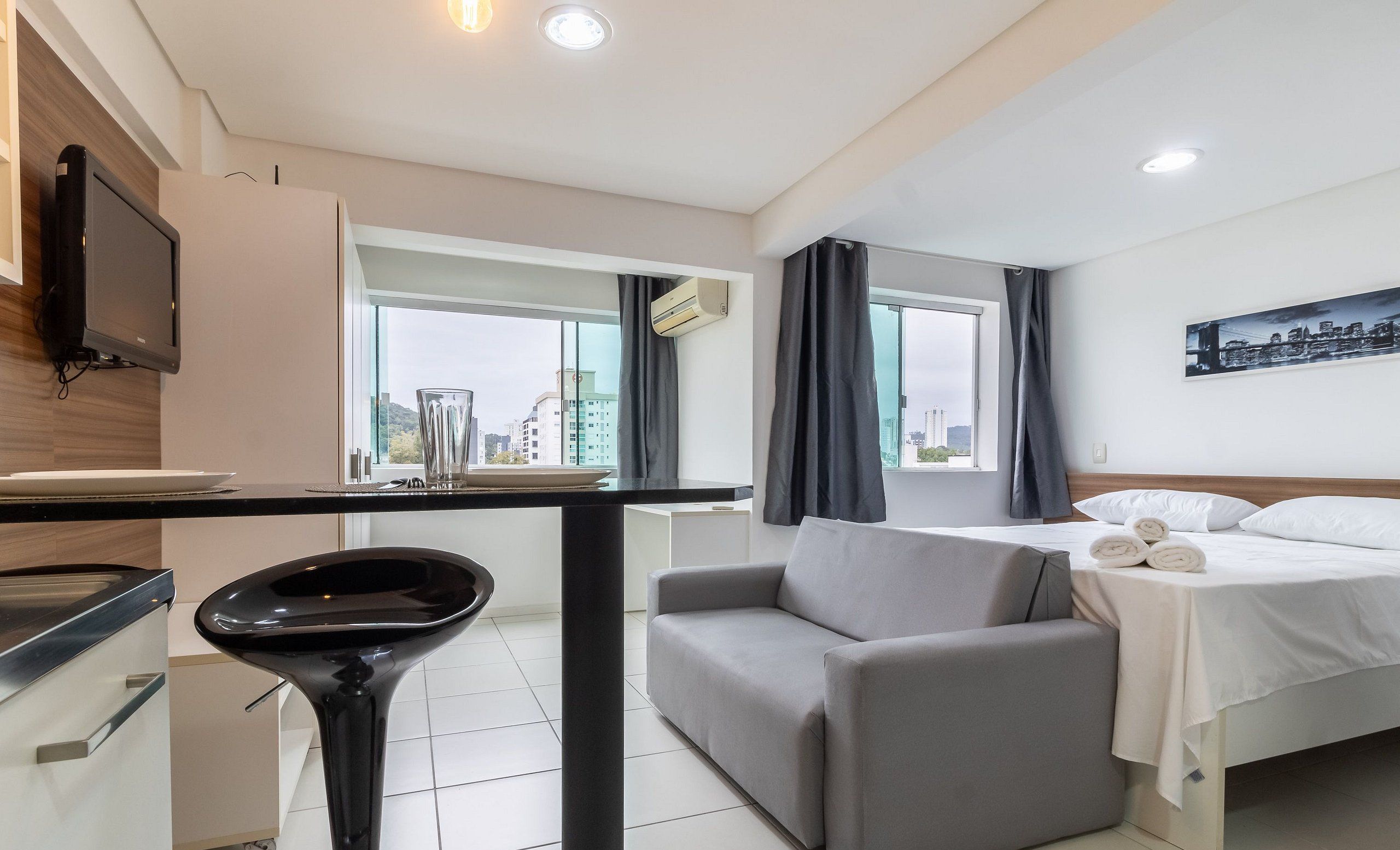 Une chambre d’hôtel moderne équipée d’un lit, d’un canapé, d’un bureau avec un téléviseur à écran plat, d’une fenêtre donnant sur la ville et d’un système de climatisation.