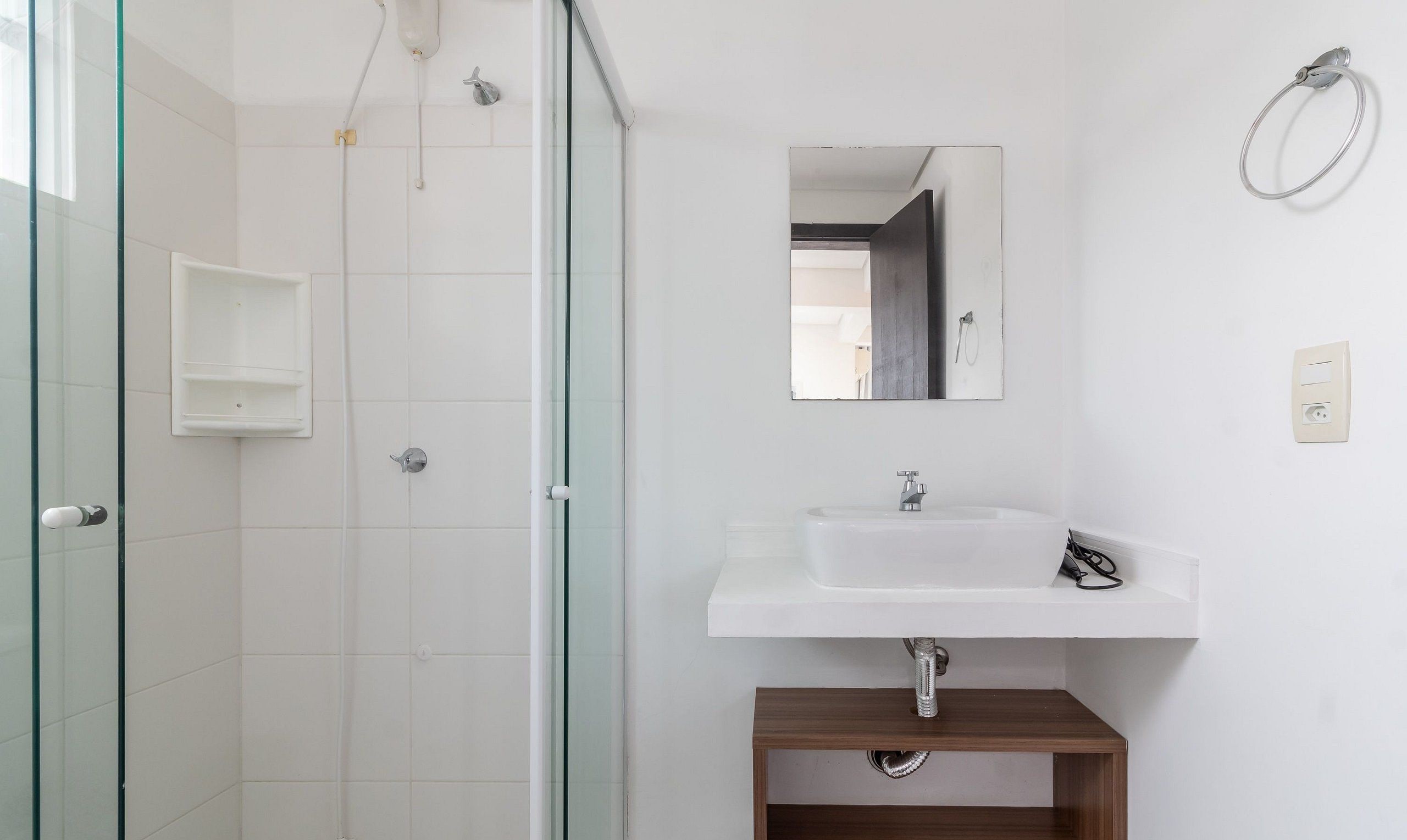Un bagno con box doccia in vetro, lavandino bianco e mobiletto in legno sottostante.