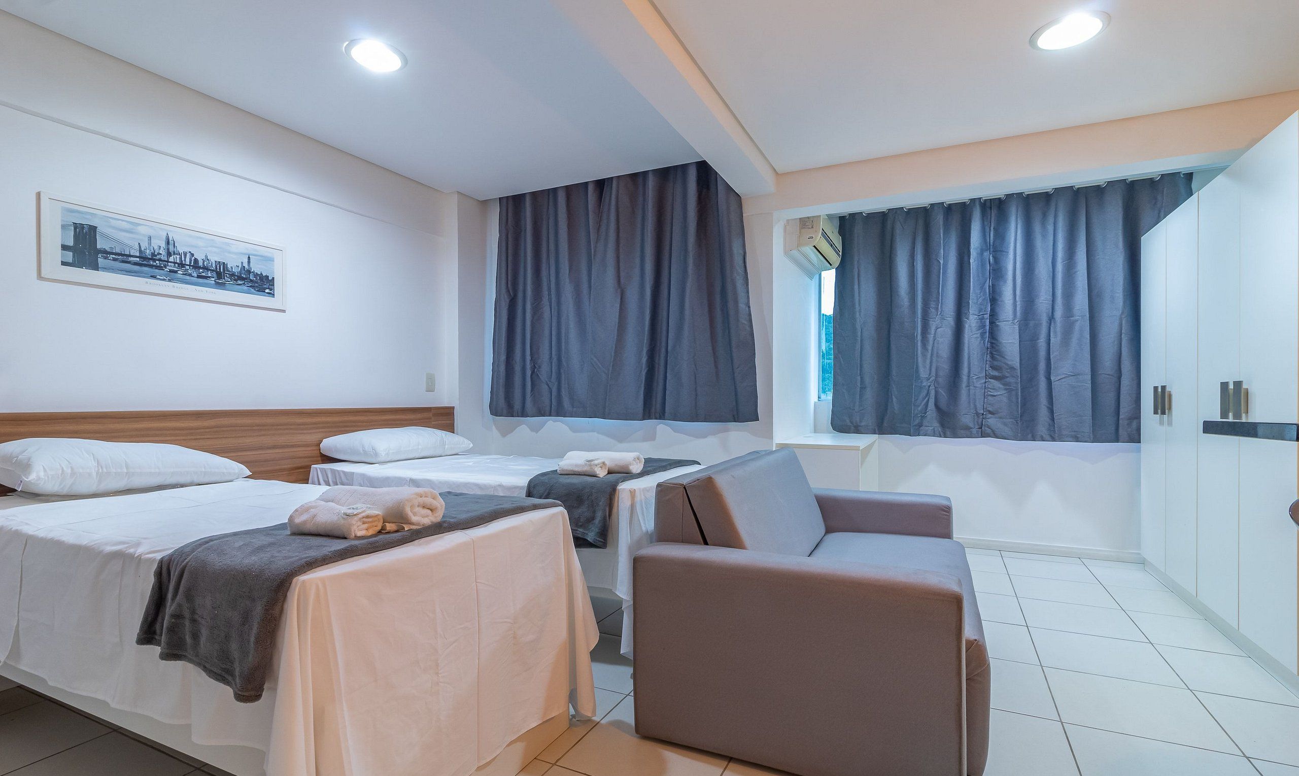 Habitación de hotel con dos camas, un sofá, una ventana con cortinas y un cuadro en la pared.