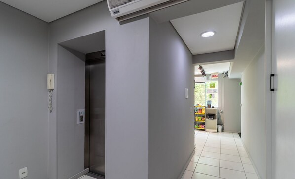 A hallway with a white tiled floor, a door with a handle, and a wall-mounted light fixture. - SPTs Studios Convenientes em Blumenau (Blumenau)