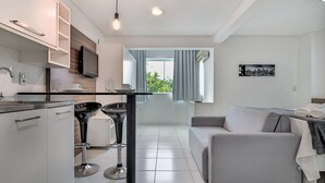 A modern kitchen with a dining area, a sofa, and a window with curtains. - SPTs Studios Convenientes em Blumenau (Blumenau)