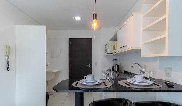 A modern kitchen with a dining table set for two, a coffee maker, and a microwave on the counter. - SPTs Studios Convenientes em Blumenau (Blumenau)