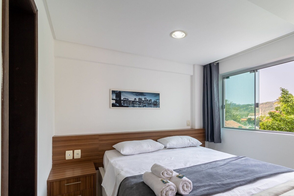Een hotelkamer met een bed, een nachtkastje, een schilderij, een raam met uitzicht en een plafondlamp.