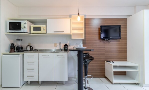 A compact kitchenette with a microwave, coffee maker, and a small TV mounted on the wall. - SPTs Studios Convenientes em Blumenau (Blumenau)