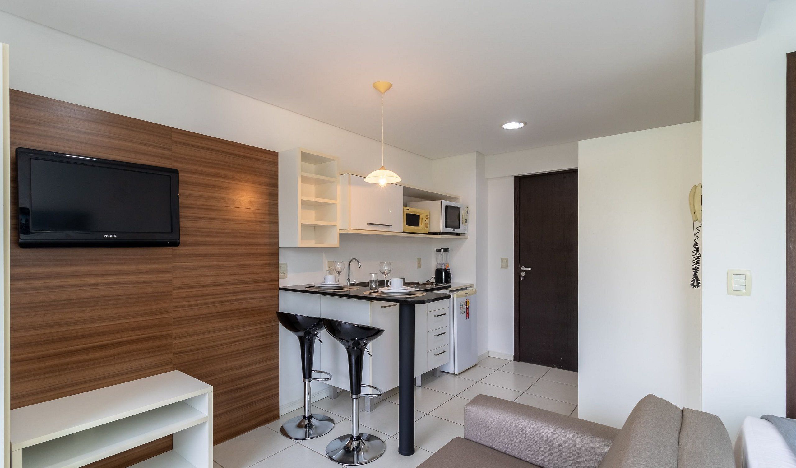 A modern kitchen with a flat-screen TV, white cabinets, and a dining area with bar stools.