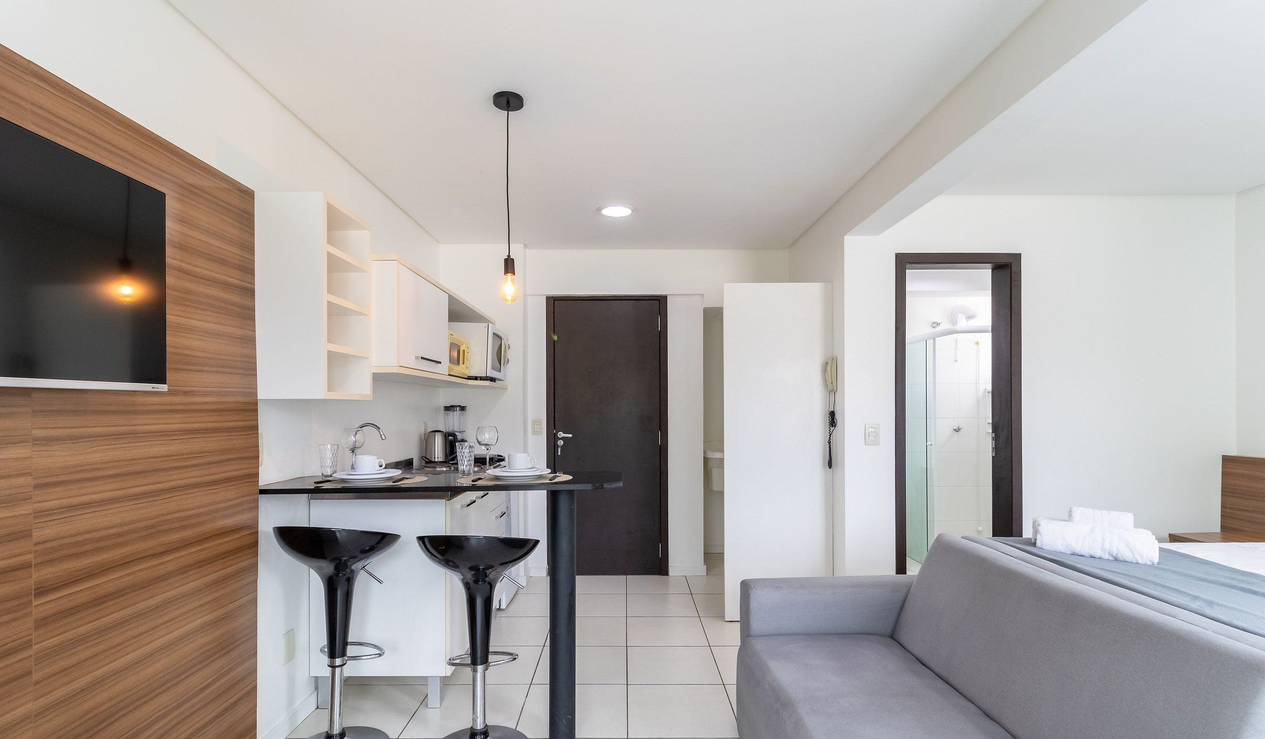 A modern kitchen with a built-in microwave, a coffee machine, and a dining area with a grey sofa and two black bar stools.
