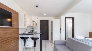 A modern kitchen with a built-in microwave, a coffee machine, and a dining area with a grey sofa and two black bar stools.
