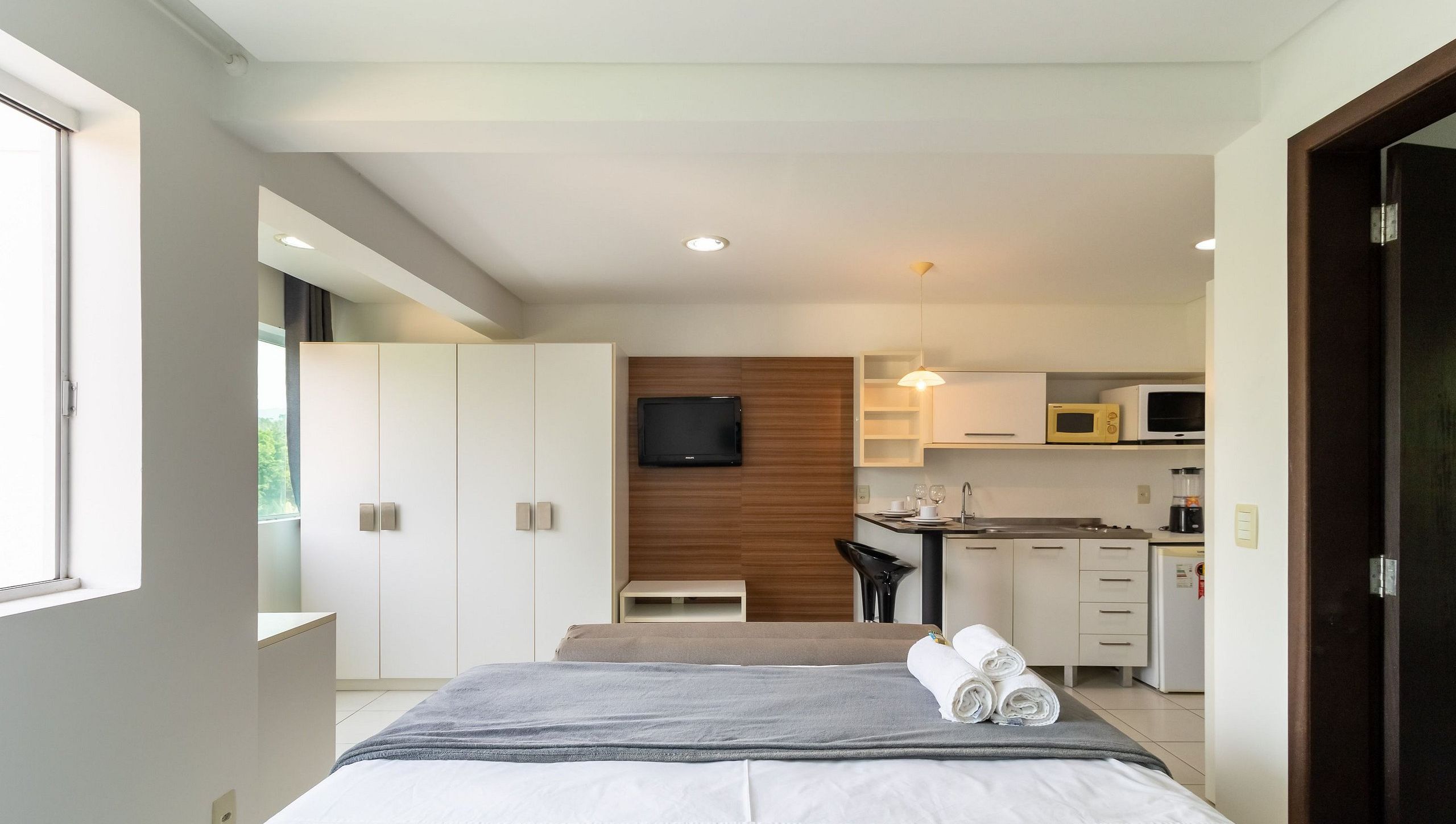 A modern bedroom with a bed, a flat-screen TV, and a kitchenette with a microwave.