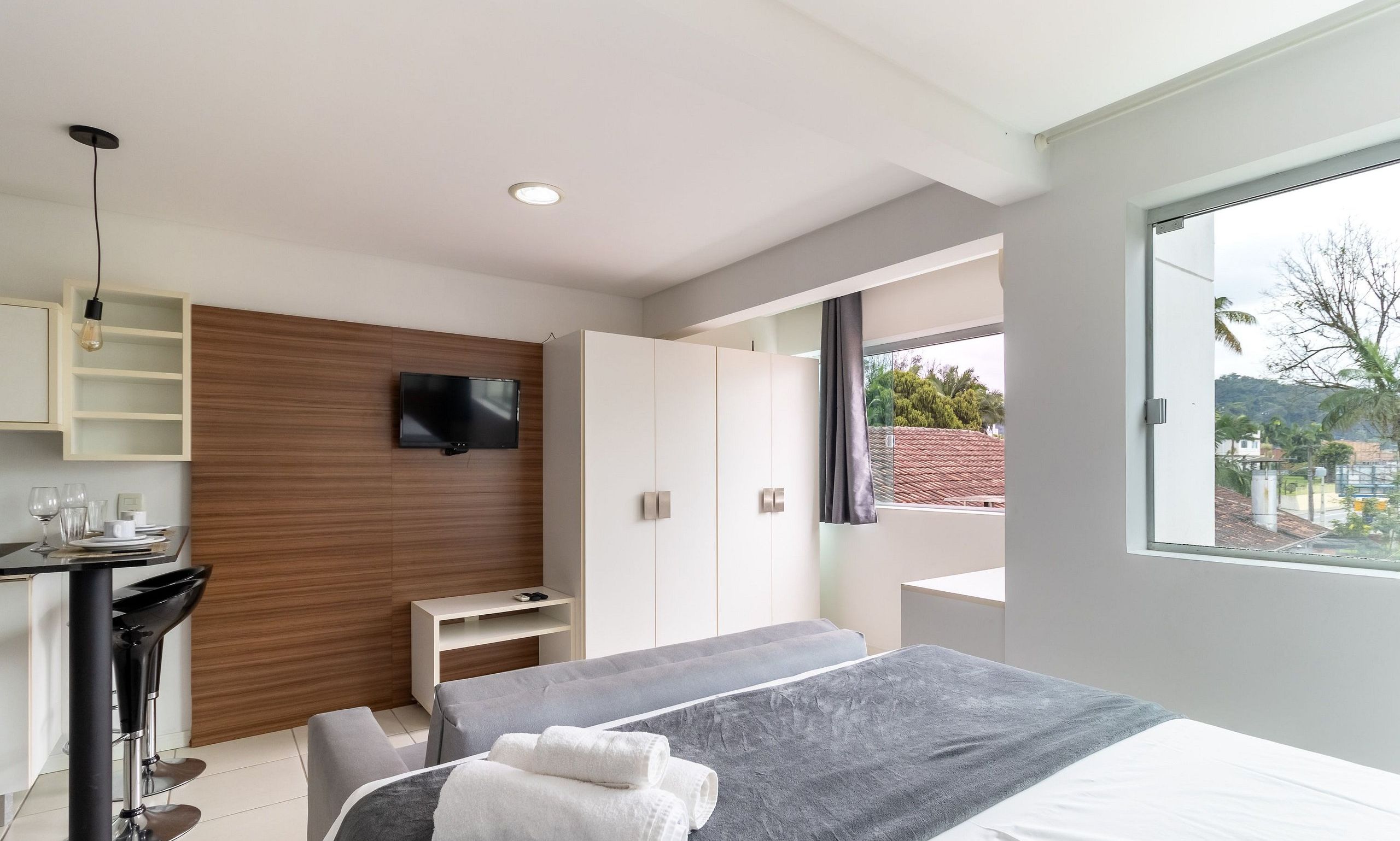 Un dormitorio moderno con cama, televisor, escritorio y ventana con vistas al exterior.