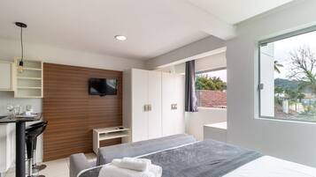 Un dormitorio moderno con cama, televisor, escritorio y ventana con vistas al exterior.
