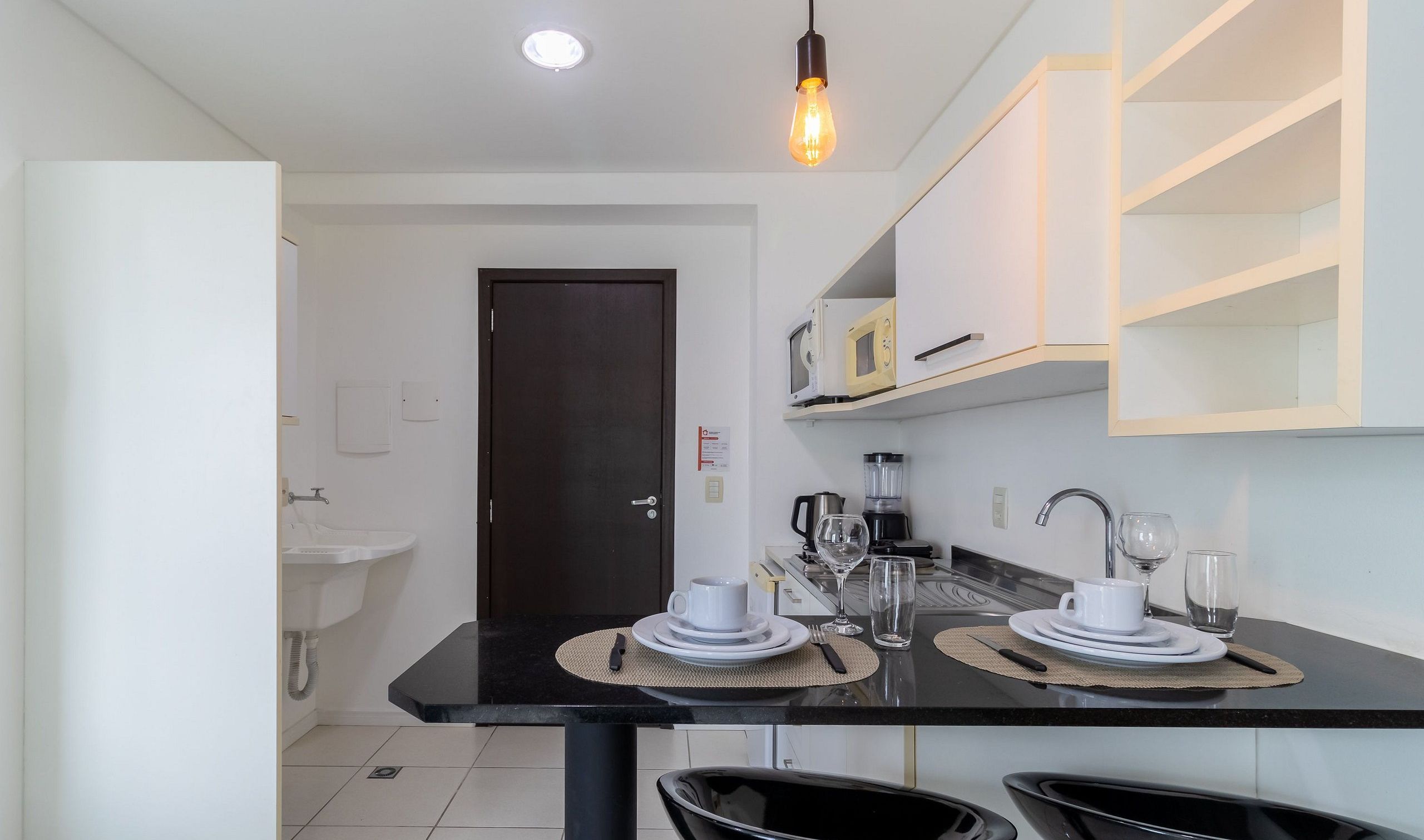 Una cocina moderna con encimera negra, armarios blancos, microondas, cafetera y lavabo.