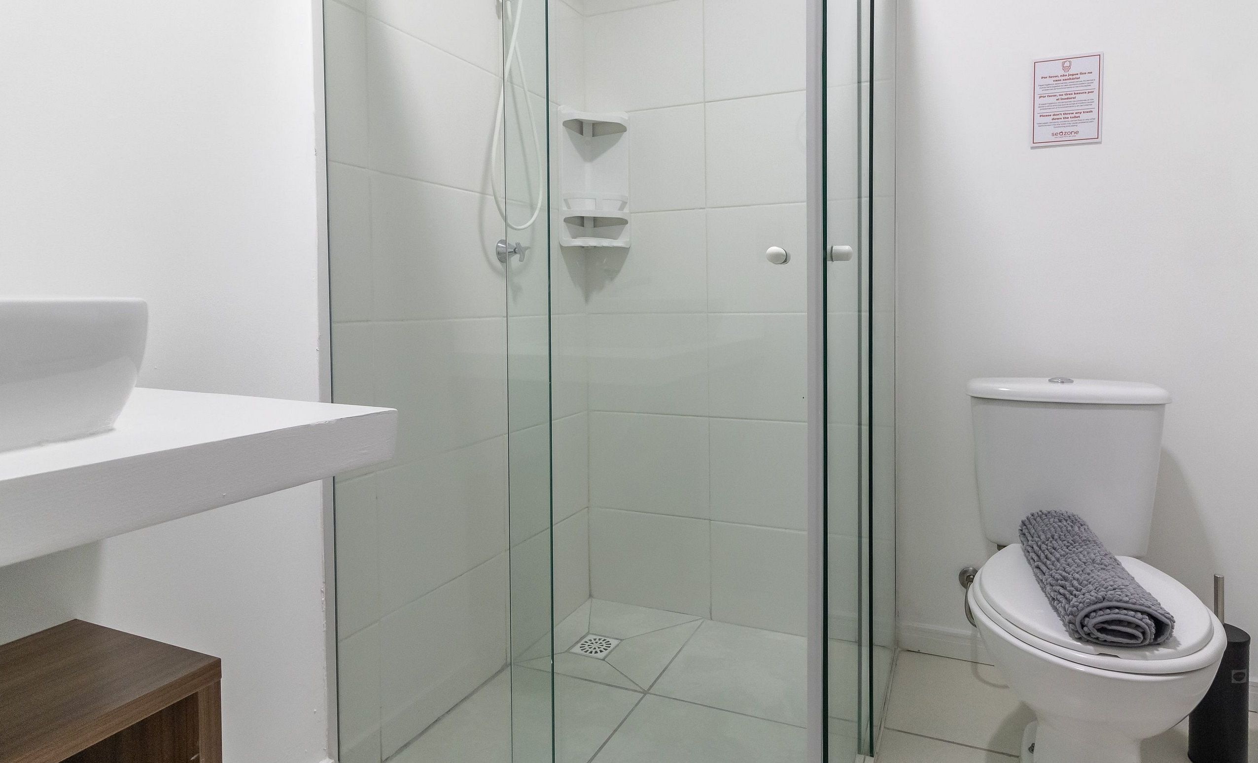 Een badkamer met een douche met glazen wand, een wit toilet en een witte wastafel.