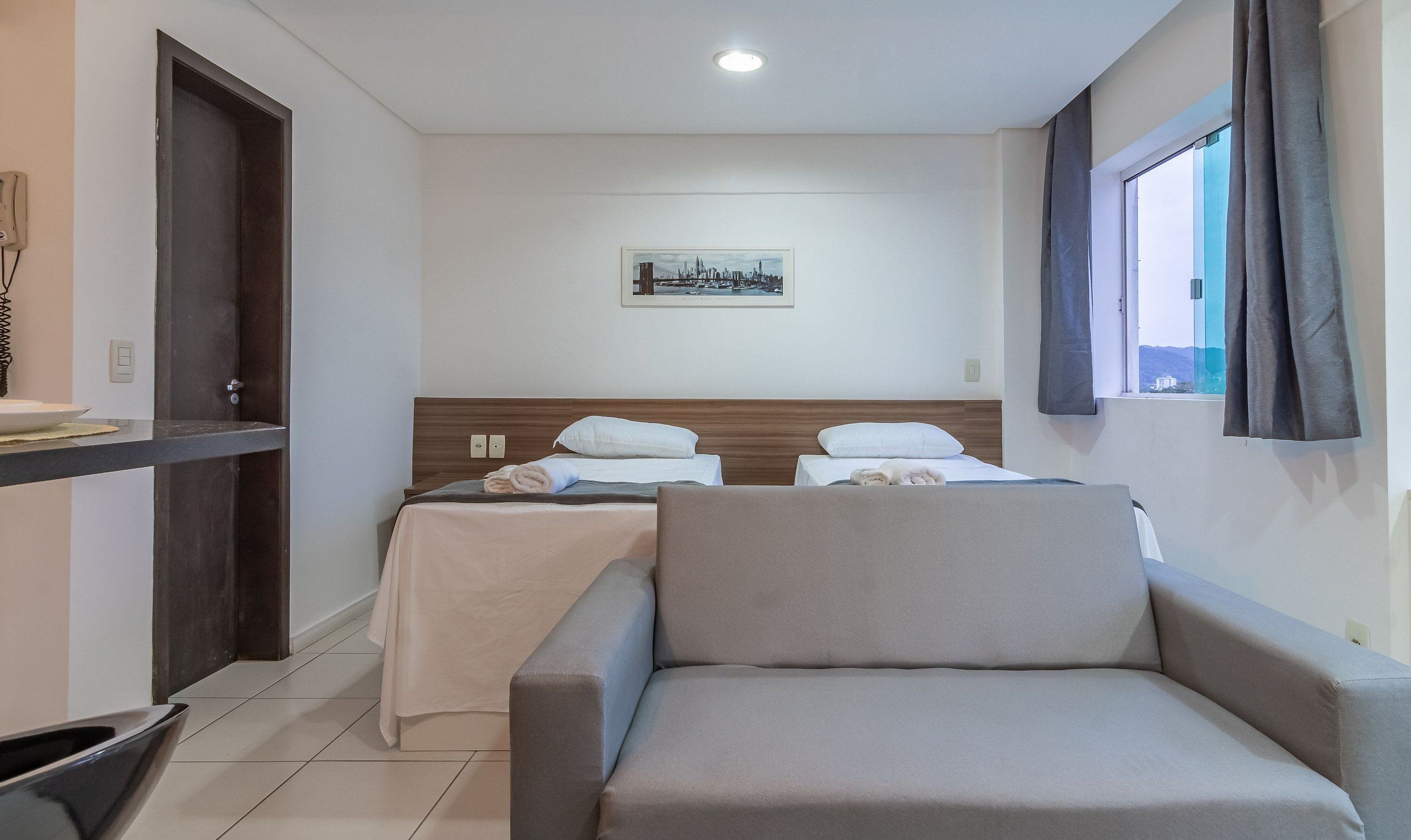 Habitación de hotel con dos camas, un sofá, una ventana con cortinas, un cuadro en la pared y un teléfono a la izquierda.