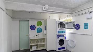 A laundry facility with a washing machine, a drying machine, and a sink. There are informational signs on the wall.