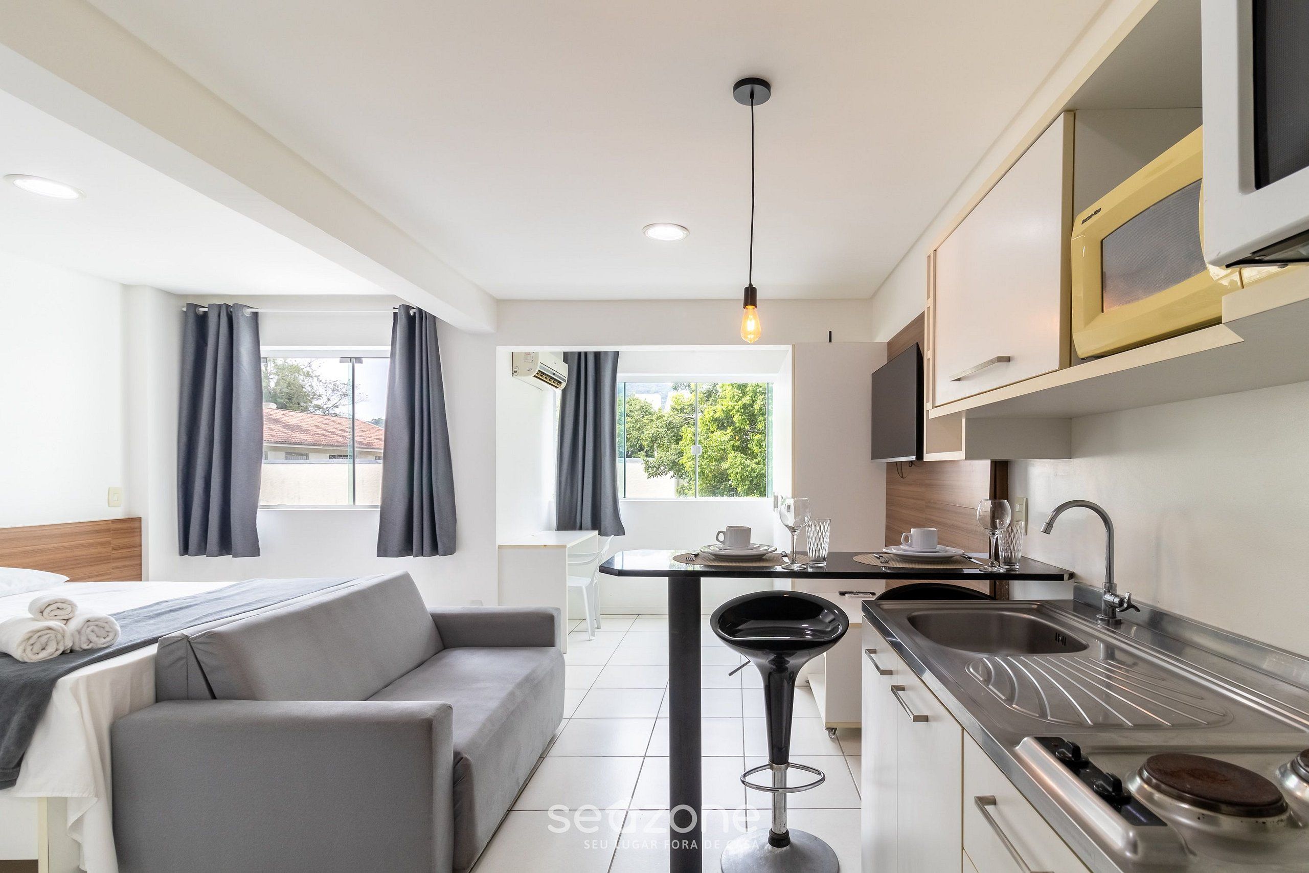A modern kitchen with a bar stool, a sink, and a microwave.