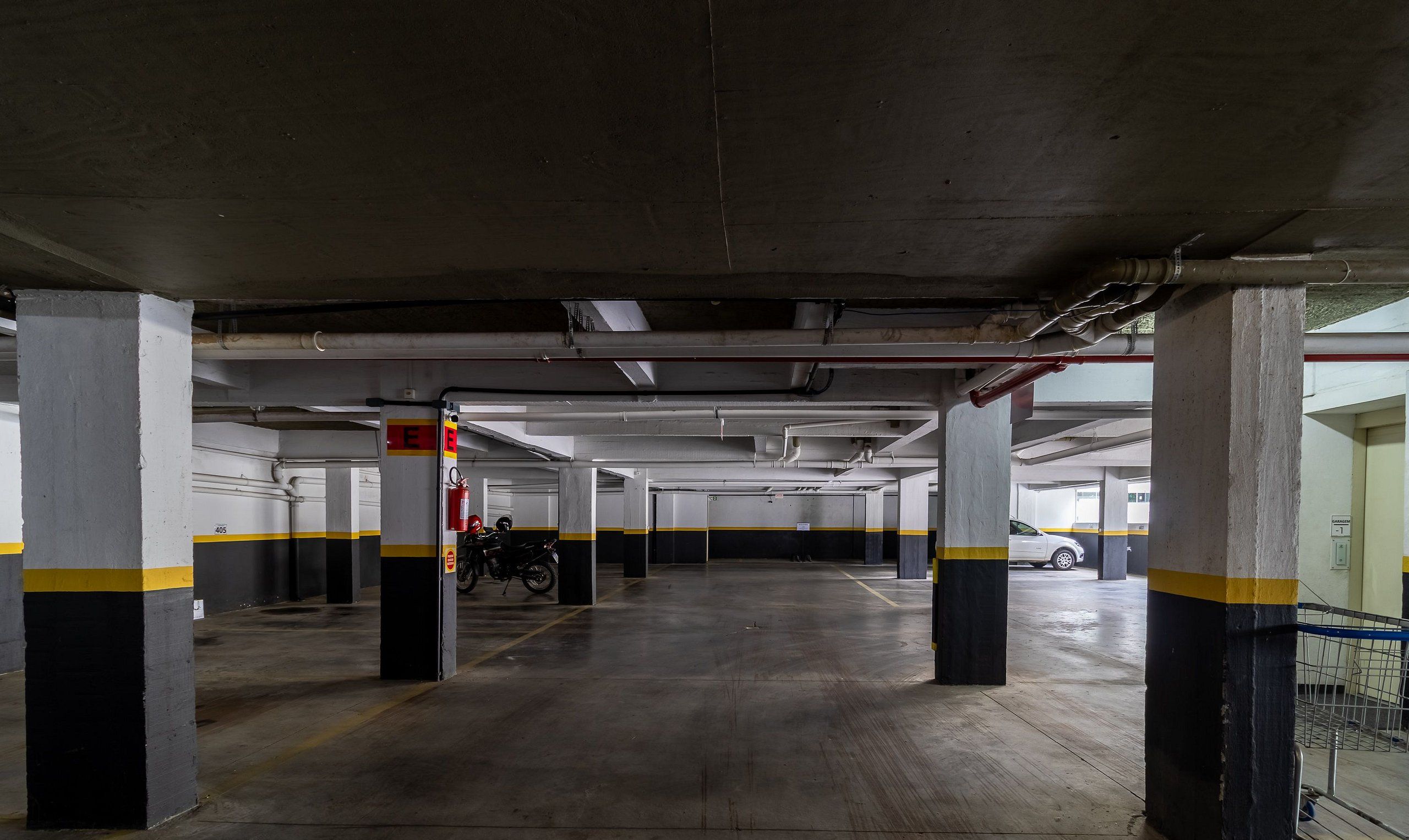 Un parking à plusieurs niveaux, doté de piliers en béton, de colonnes rayées de jaune et de noir, et d’un extincteur fixé à l’un des piliers.