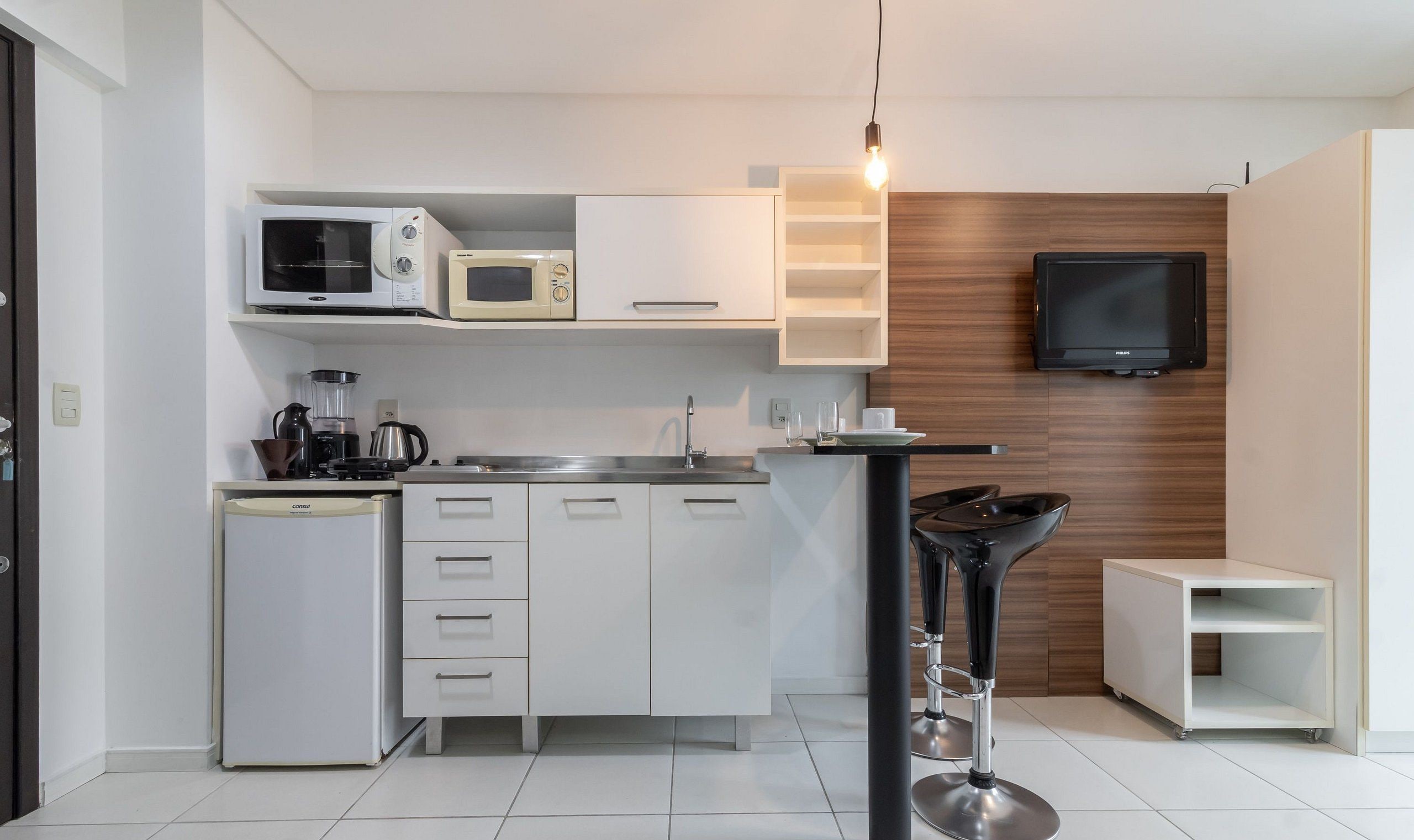 Una cocina moderna con armarios blancos, una cafetera, un microondas, un lavaplatos y un taburete negro.