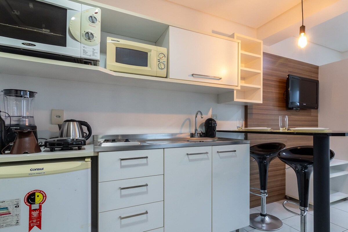 A modern kitchen with white cabinetry, a built-in microwave, a coffee maker, and a black bar stool.