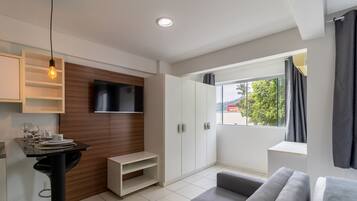 A modern living room with a flat-screen TV, a dining area with a table set for two, and a large window with a view.