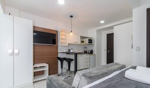 A modern hotel room with a bed, a desk, a kitchenette, and a TV. - SPTs Studios Convenientes em Blumenau (Blumenau)