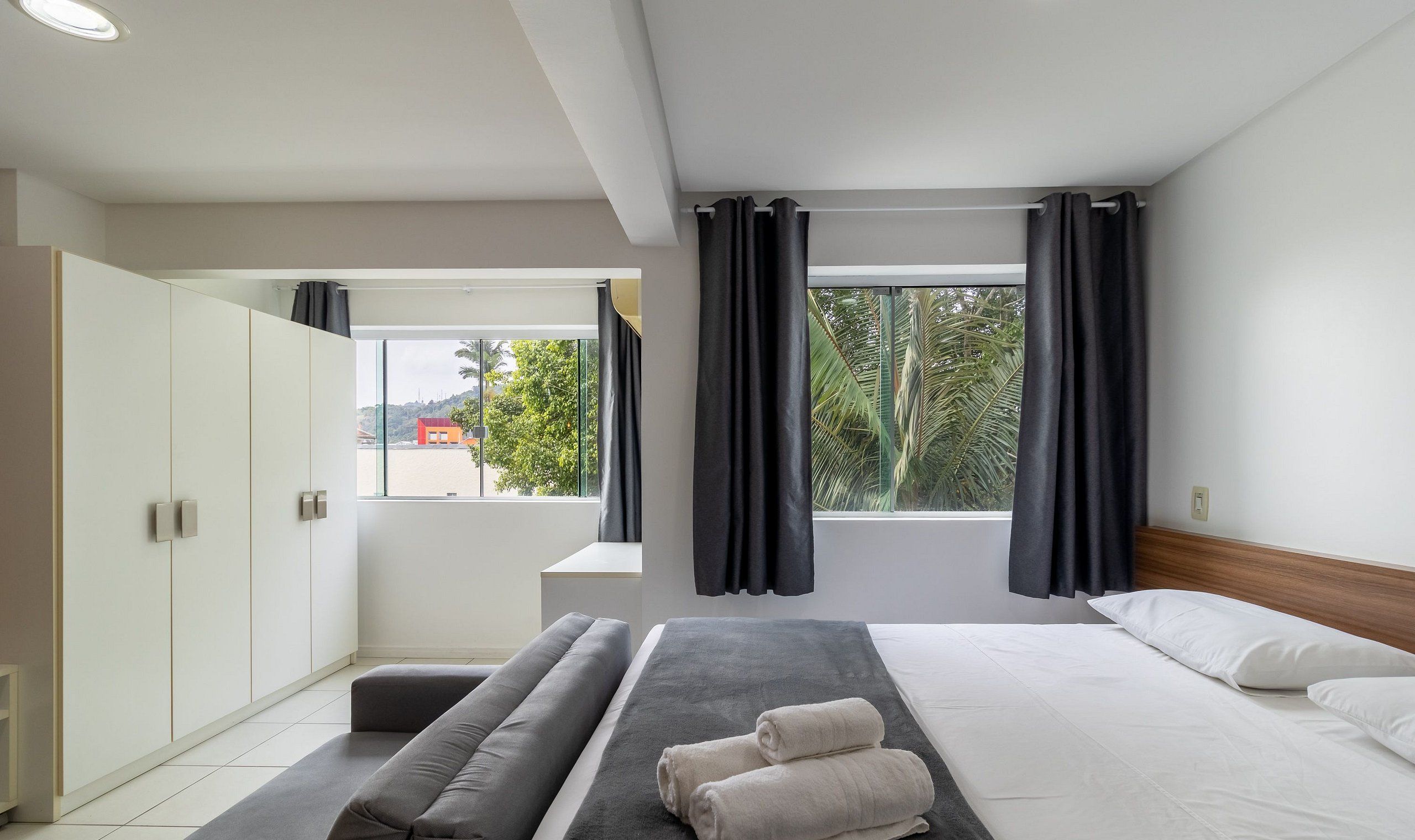 Une chambre d’hôtel moderne équipée d’un lit, d’un coin salon, d’une armoire et d’une fenêtre avec des rideaux.