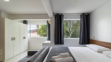 A modern hotel room with a bed, a seating area, a wardrobe, and a window with curtains.