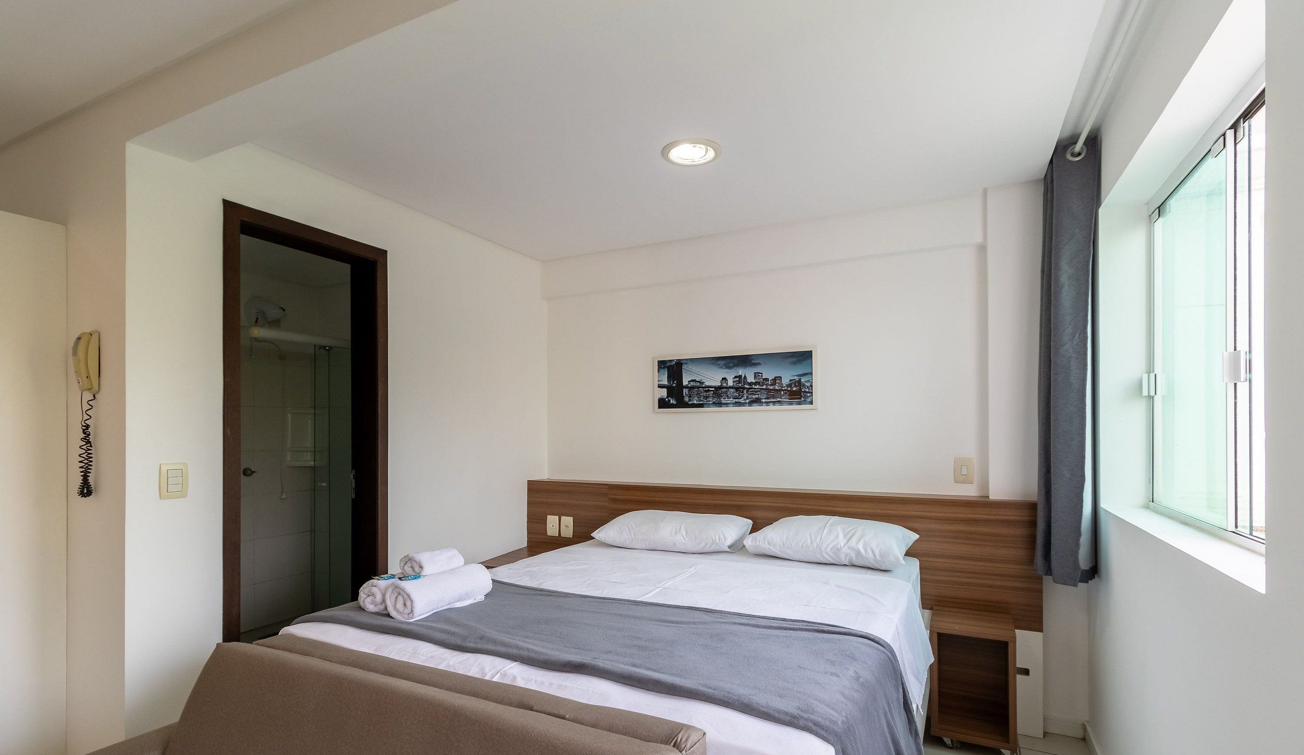 Een hotelkamer met een bed, een schilderij aan de muur, een telefoon aan de wand en een raam.