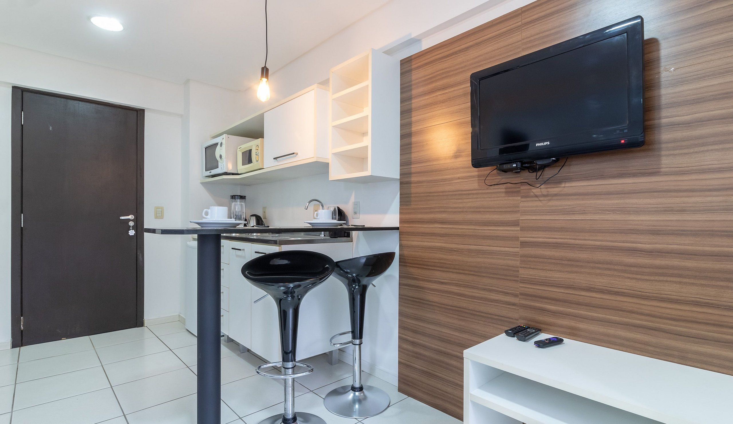 A modern kitchen with a microwave, coffee maker, and a TV mounted on the wall.