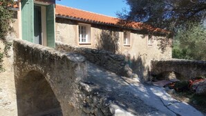 A rustic stone bridge leading to a traditional building with a tiled roof and green shutters.