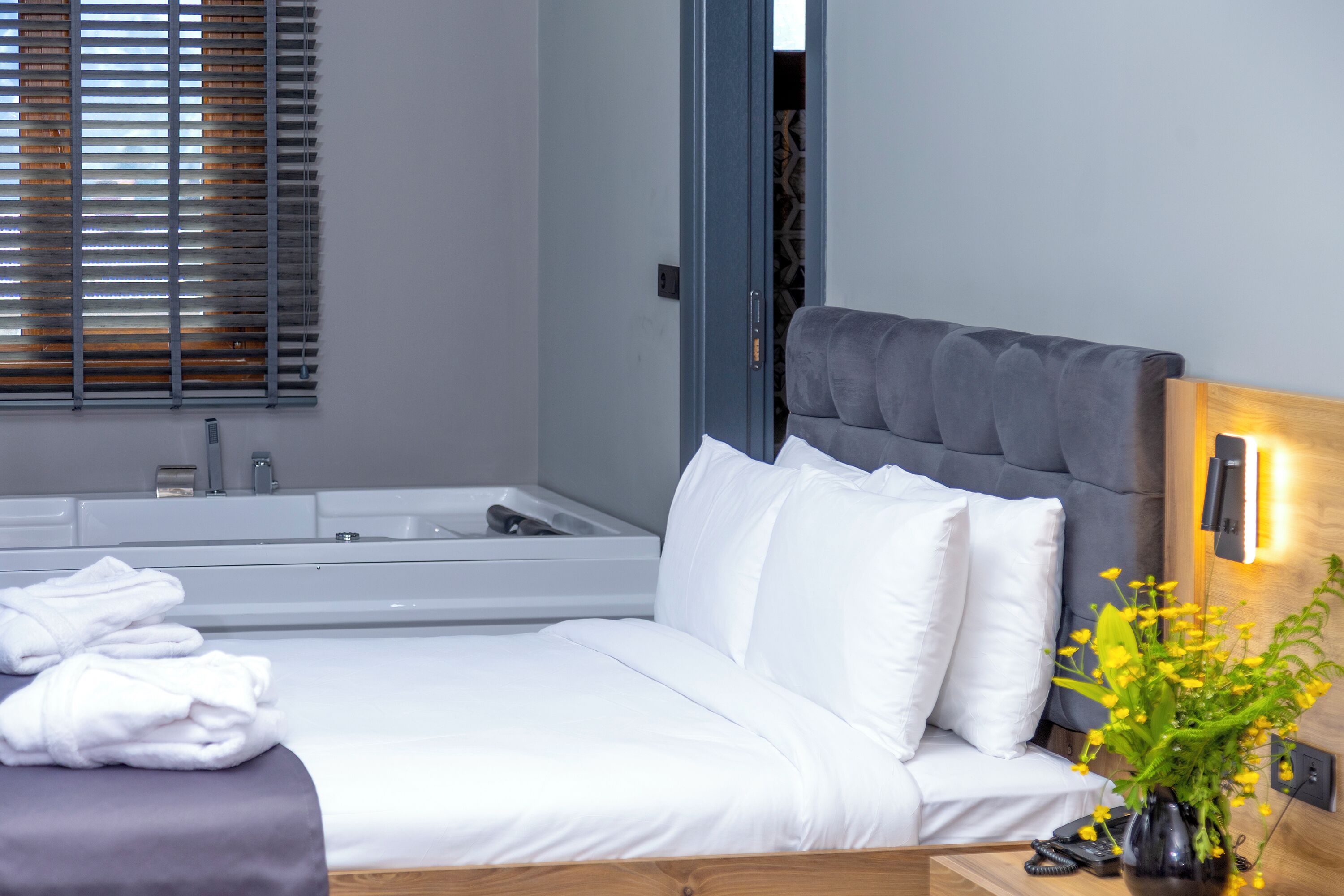 A modern hotel room with a large bed, a bathtub, and a bedside table with a vase of flowers.