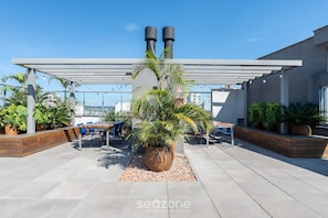 Une terrasse sur le toit agrémentée d’un grand pot de fleurs, de meubles d’extérieur et d’une structure en forme de pergola.
