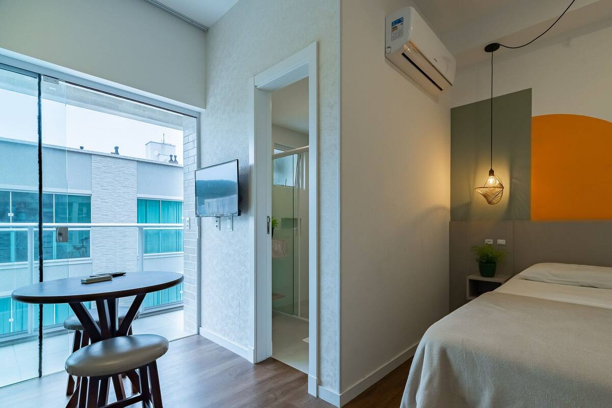 Quarto de hotel com varanda, cama, televisão e luminária moderna.