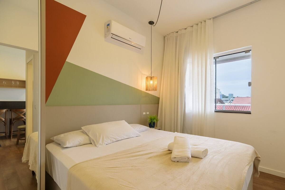Quarto de hotel com uma cama, uma escrivaninha e janela com vista para edifícios.