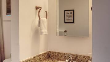A bathroom with a granite countertop sink, a towel rack, a mirror, and a framed sign on the wall.