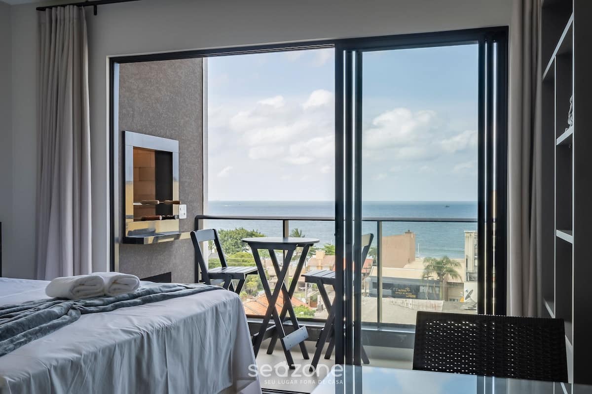 Ein Hotelzimmer mit großem Balkon, einem Bett mit ordentlich gemachtem Bett, einem kleinen Tisch und Stühlen sowie Meerblick.