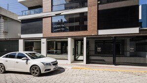 A modern building with a double entrance, numbered 141 and 142, and a white car parked in front. - VFR Estudios proximos a praia de Bombas (Bombinhas)