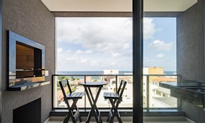 A balcony with a table and chairs, a TV, and a view of the city and sea. - VFR Estudios proximos a praia de Bombas (Bombinhas)