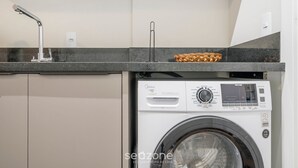 A compact laundry area with a washing machine, a sink, and a woven basket on the countertop. - VFR Estudios proximos a praia de Bombas (Bombinhas)